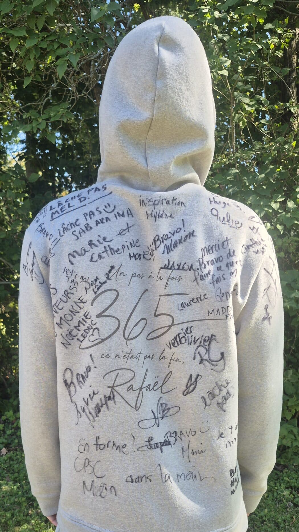 The back of the grey hoodie, covered in marker: names, hearts and notes — Lâche pas, Bravo!, Inspiration, En forme!, CPSC Main dans la main — written all around the printed Un pas à la fois, 365, ce n'était pas la fin, Rafaël.