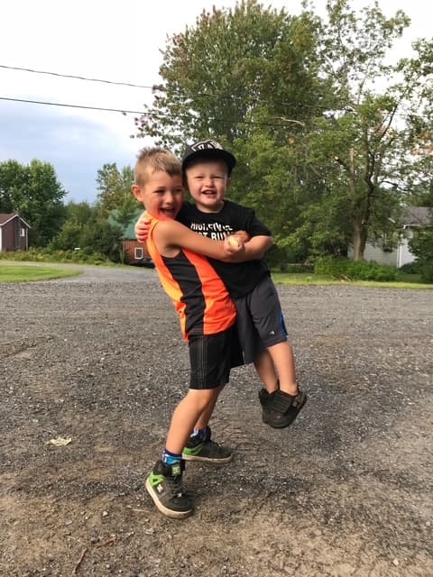 Rafaël qui rit pendant que son grand frère Maksim le serre et le soulève de terre dans l'entrée de gravier.