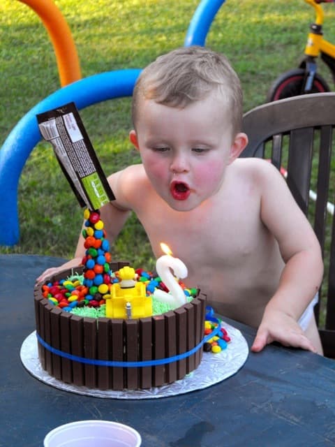 Rafaël penché sur son gâteau, les joues gonflées, en train de souffler la chandelle en forme de deux.