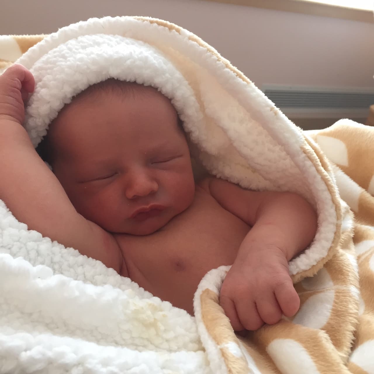 Rafaël à quelques jours, endormi dans une couverture blanche en peluche, un petit poing levé à côté de sa tête.